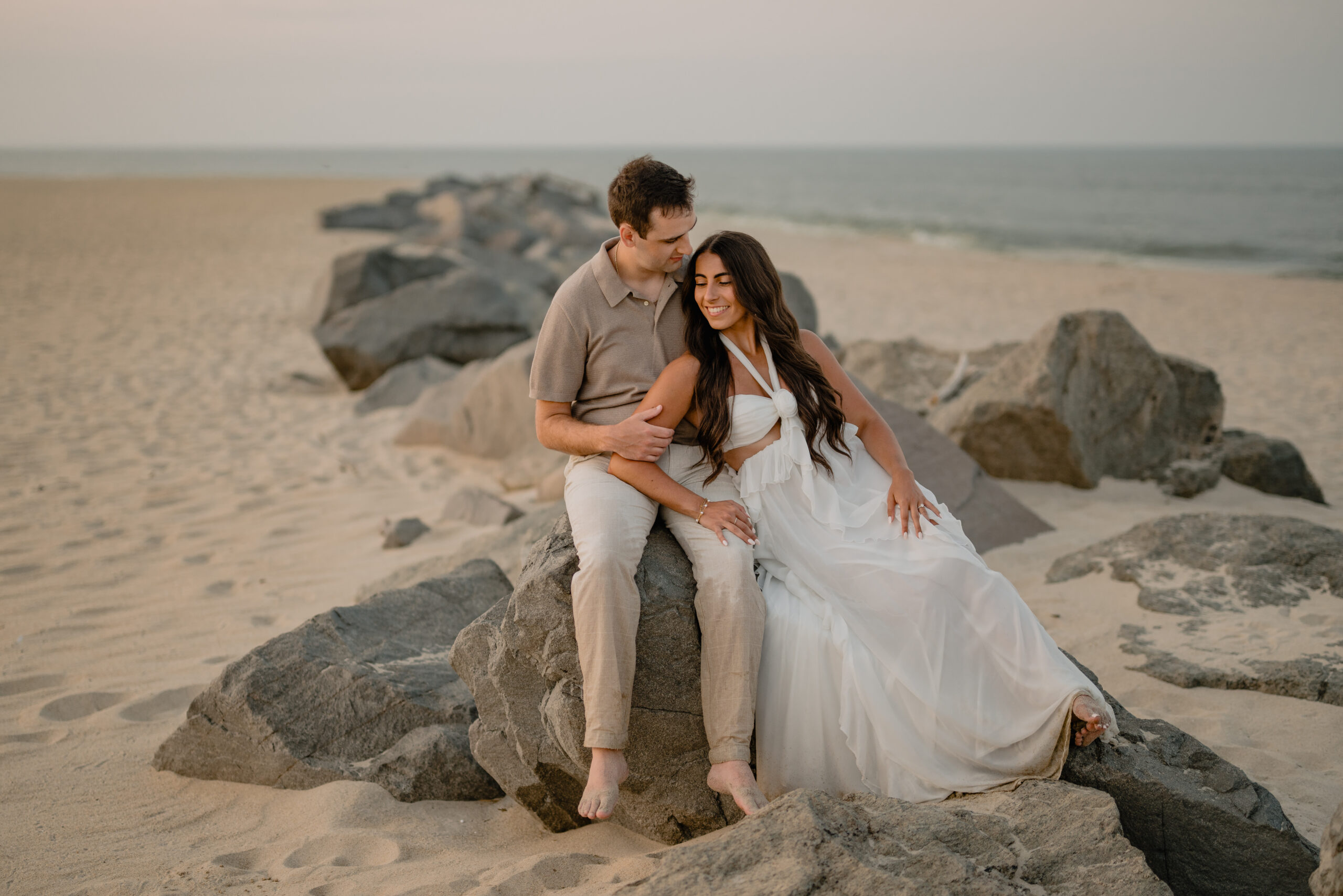 Couple sitting by a rock during their Deep Cut Gardens & Sandy Hook Beach Engagement Session